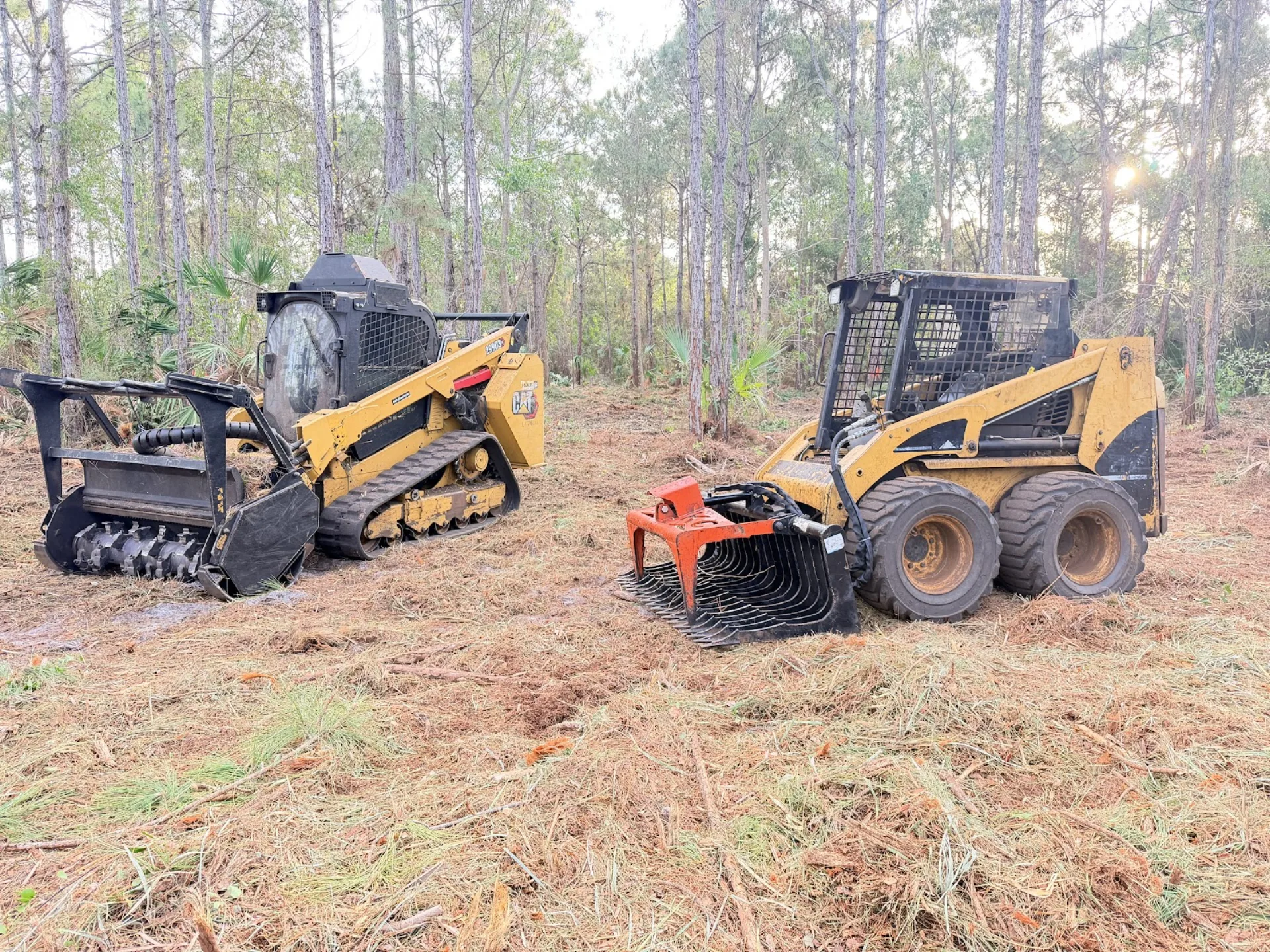 Two tracked skid steers with mulching head and grapple on freshly cleared Florida ground